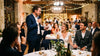 Témoin debout au micro pendant un repas de mariage, une feuille à la main, les mariés l'écoutent