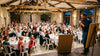 Salle des fêtes avec 80 invités attablés, un animateur au micro devant un paperboard